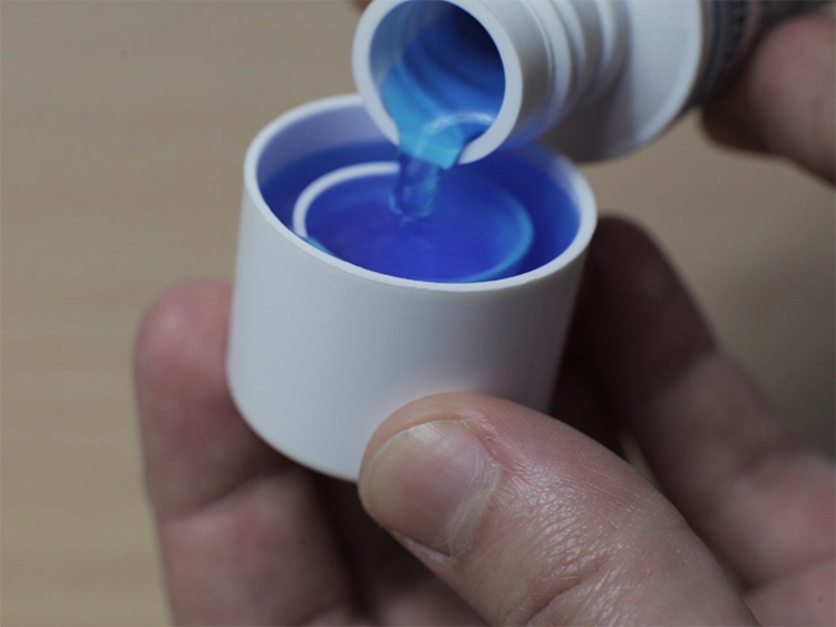 Close up of hand pouring blue liquid into a bottle cap