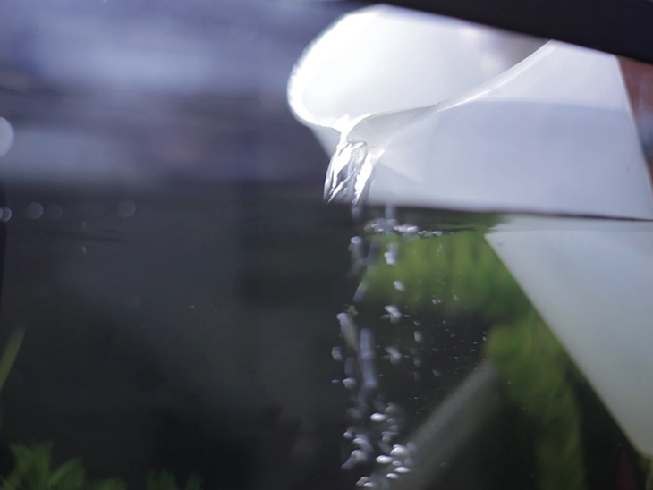 A jug pouring water slowly into a partially full aquarium