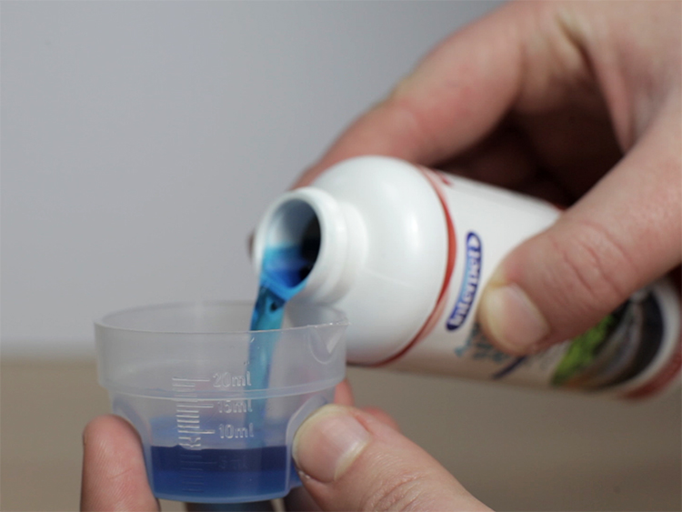 Close up of a hand pouring blue fish medicine into a transparent measuring cap
