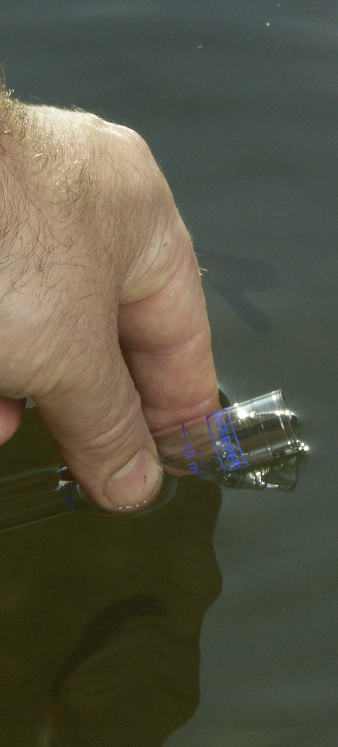 Hand filling up a plastic vial with pond water